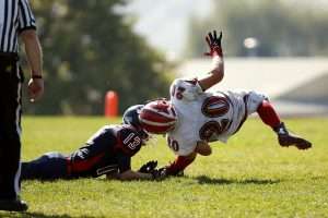 A football player in white football gloves gets tackled during an intense game.