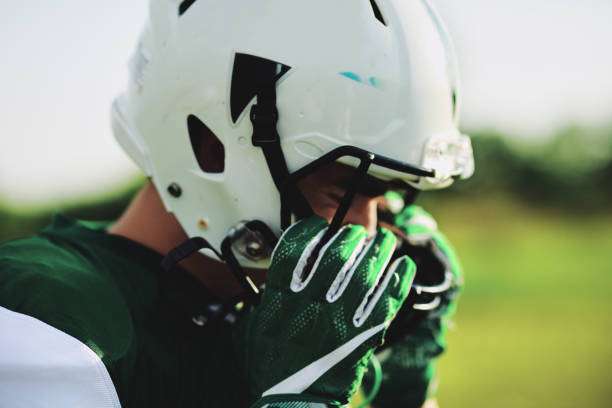 Football player adjusting his green football gloves and white helmet on the field.