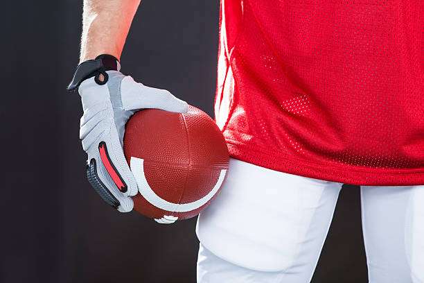 Close-up of a player in a red jersey holding a football with grey football gloves.