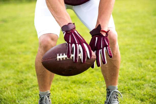 Player wearing maroon football gloves holding the ball on a green grass field.
