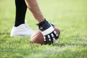 Player in black and white football gloves setting the ball on green grass.