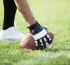 Player in black and white football gloves setting the ball on green grass.