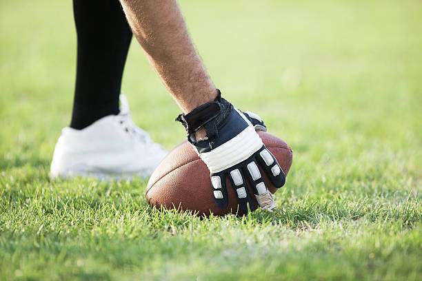 Player in black and white football gloves setting the ball on green grass.