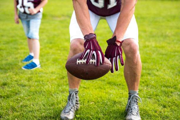 A football player in maroon uniform and football gloves preparing to snap the football.