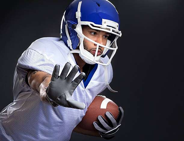 Football player in blue helmet, white jersey, and black football gloves ready to block.